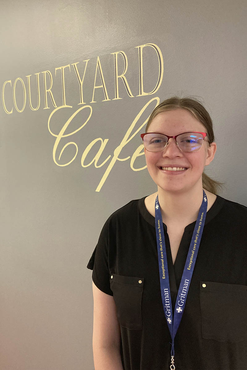 Portrait of a woman standing in front of a courtyard cafe sign.