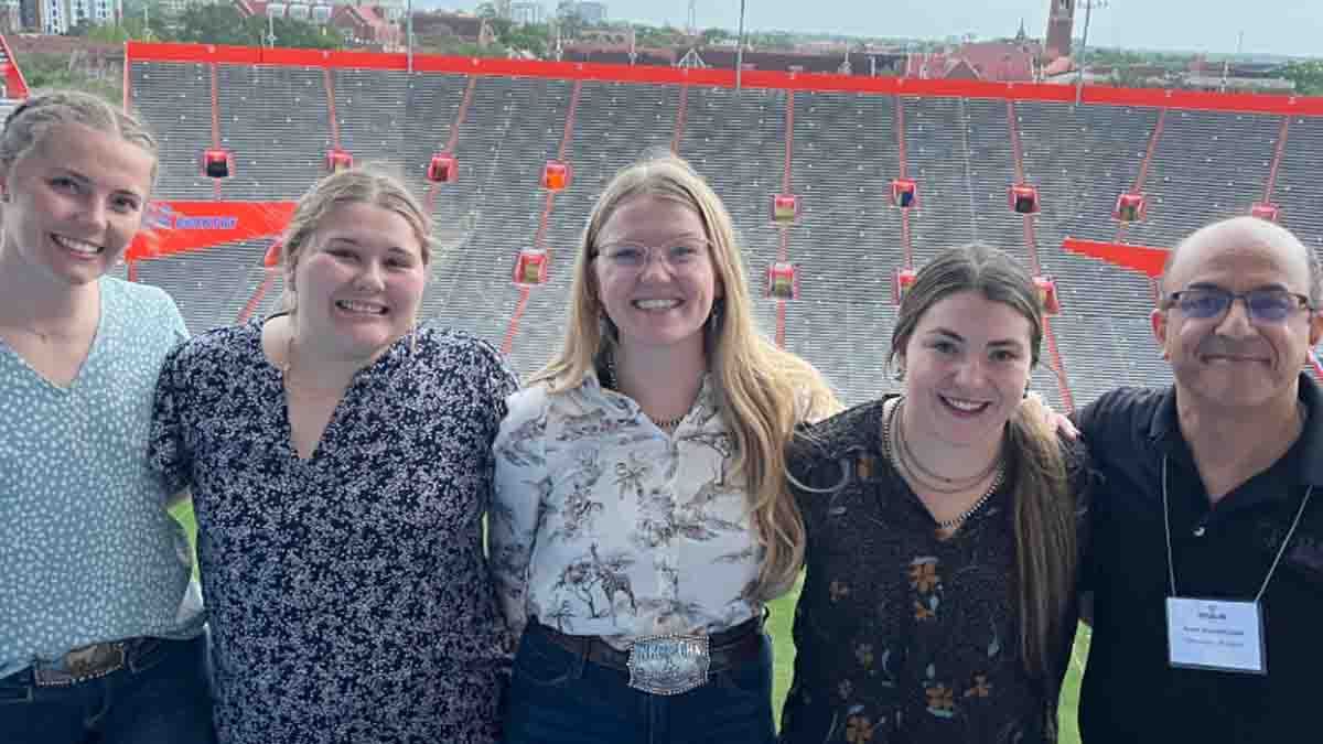 A group photo of four women and a man with a stadium in the background.