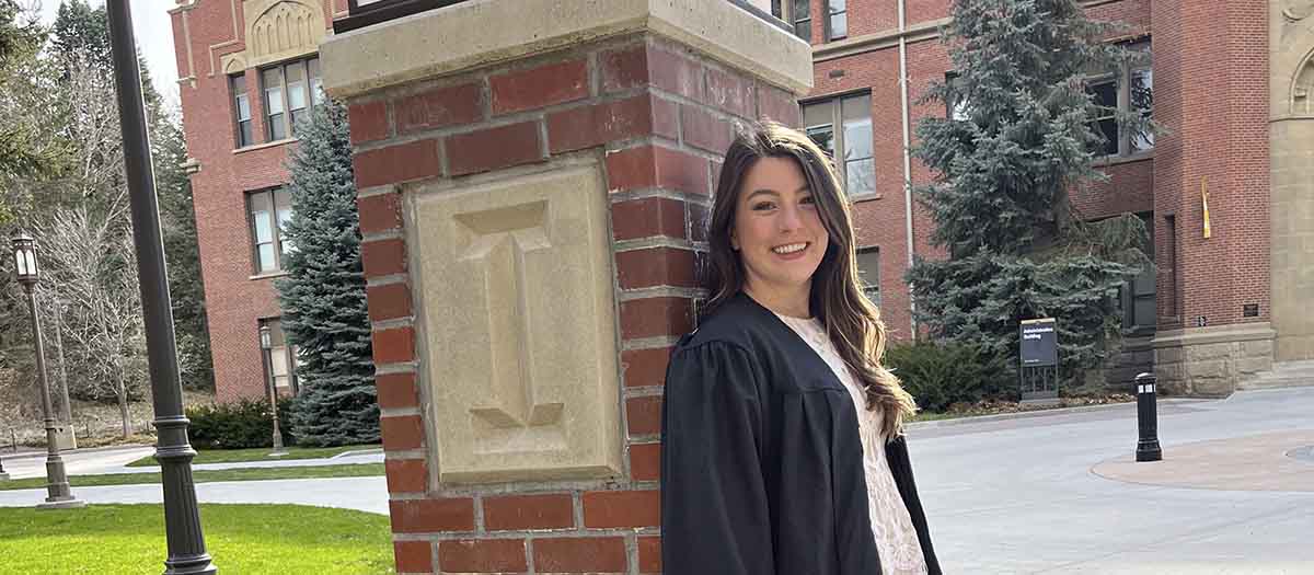 A woman leaning against a red brick post with the letter I carved into it.