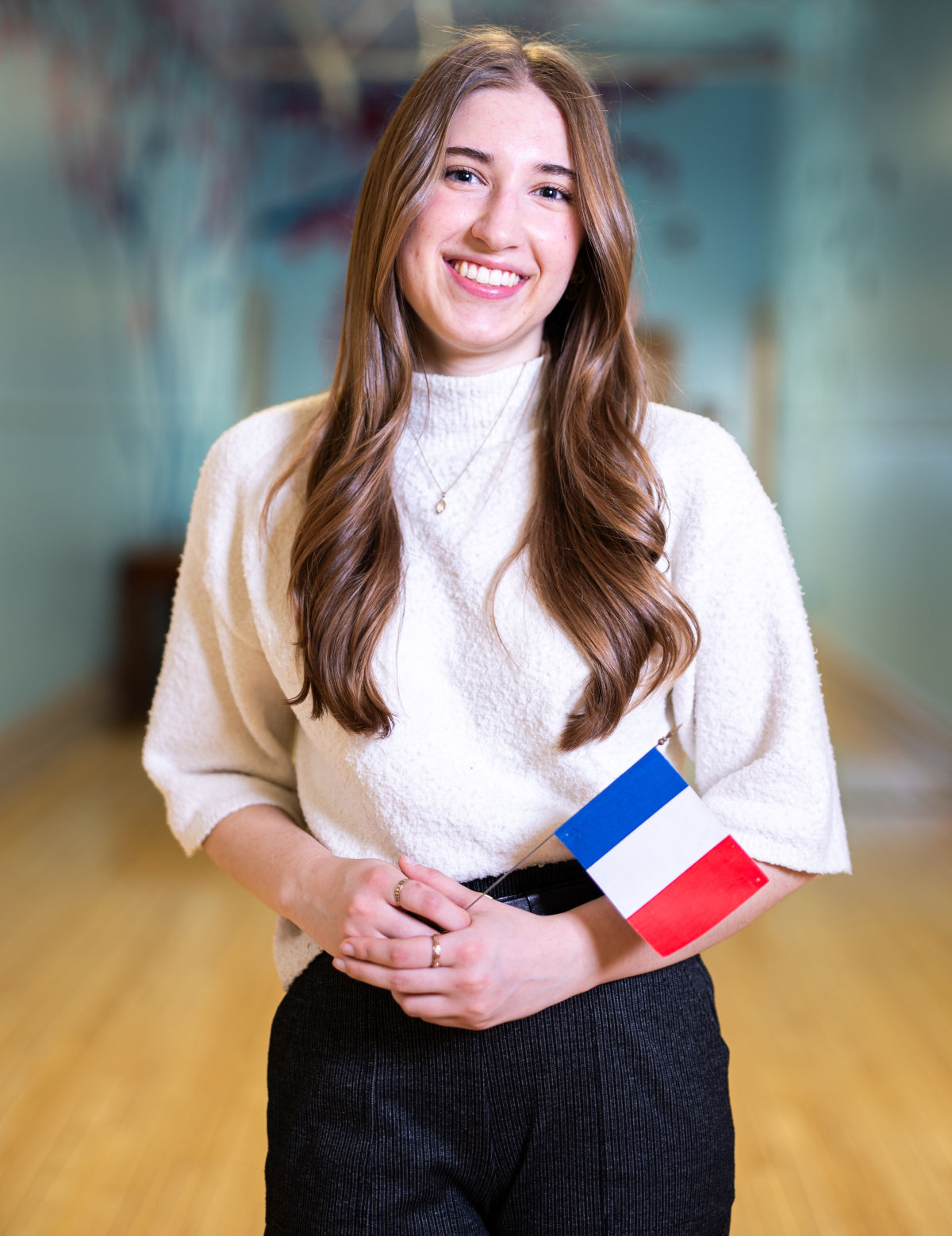 Woman standing in a hallway holding a blue, white and red flag.