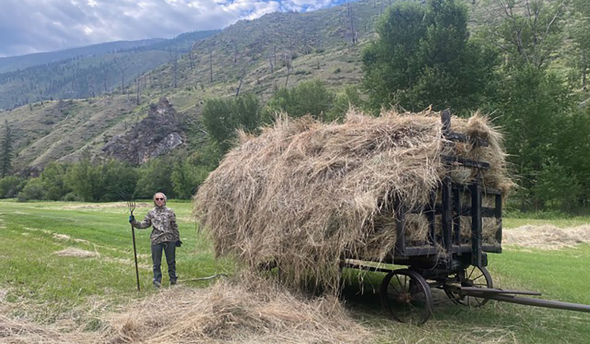 A person stands next to a wagon full of hay.