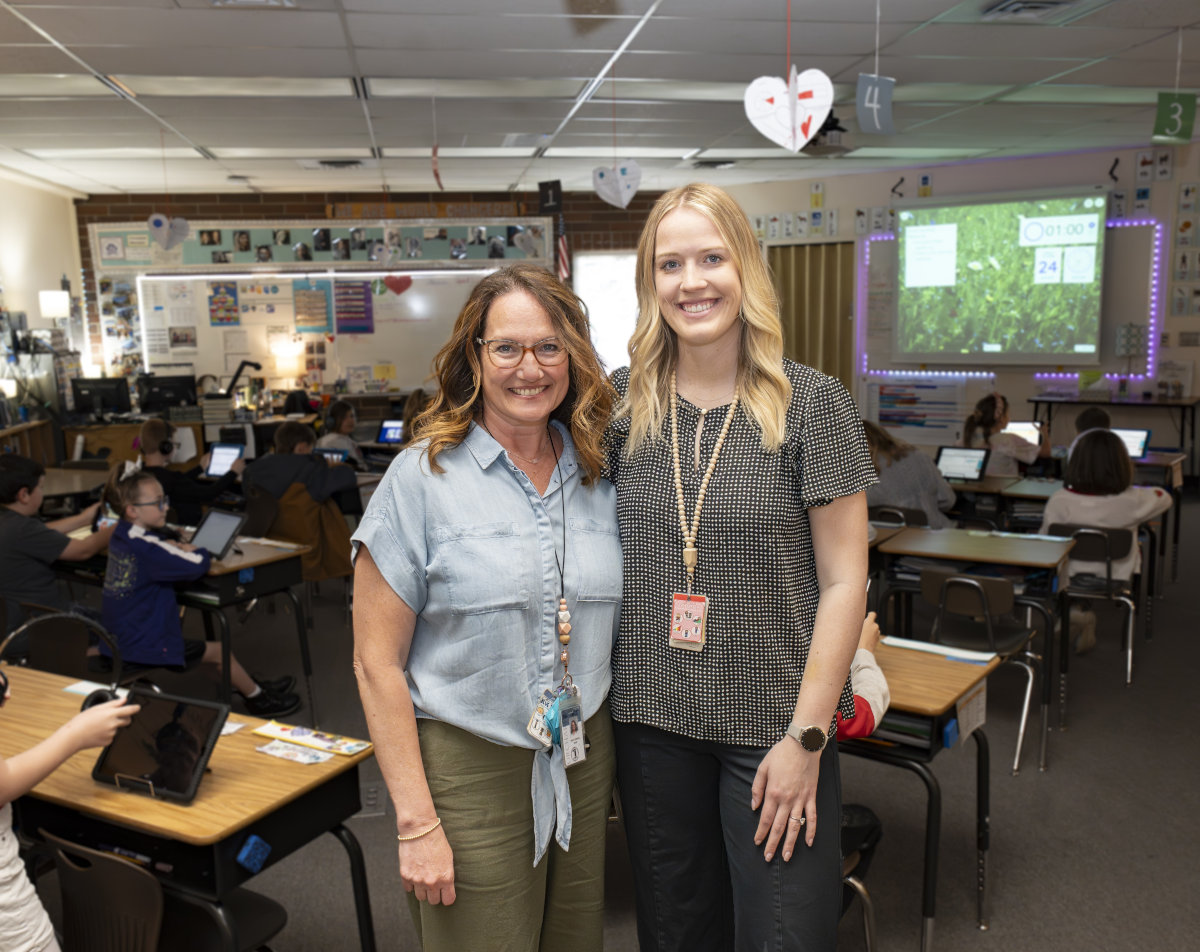 Portrait of a smiling blond woman and a brown-haired woman with glasses in a school classroom.